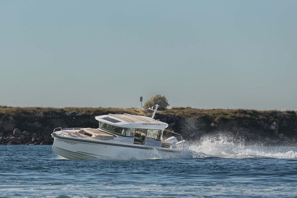 The yacht Calypso speeding with a rocky hill and a tree in the background