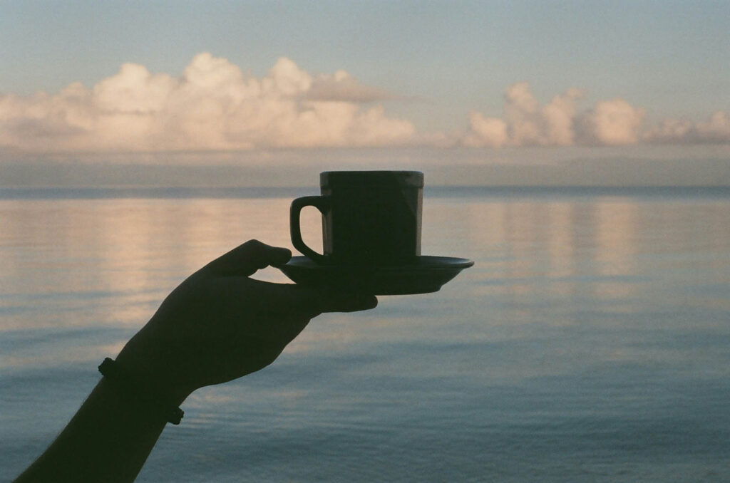 Hand holding a coffee mug with the sea in the background